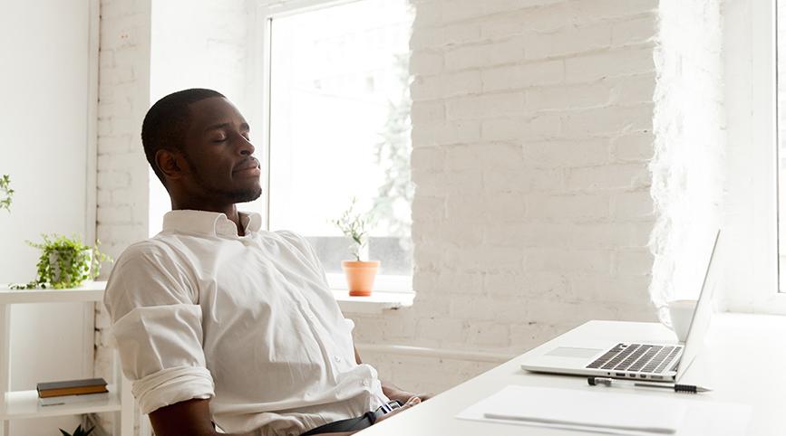 一个黑人男性闭着眼睛坐在办公桌前沉思.