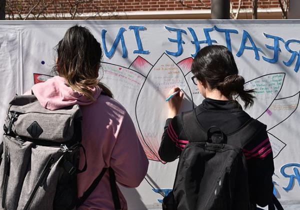 Two students standing, writing on a large board.