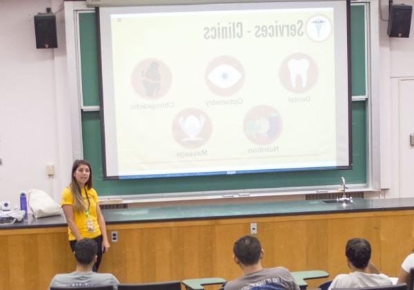 A student in a yellow polo standing in front of a screen with a health services presentation.