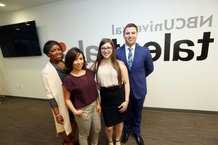 Four students wearing business attire stand in front of a wall with an NBC Universal sign.